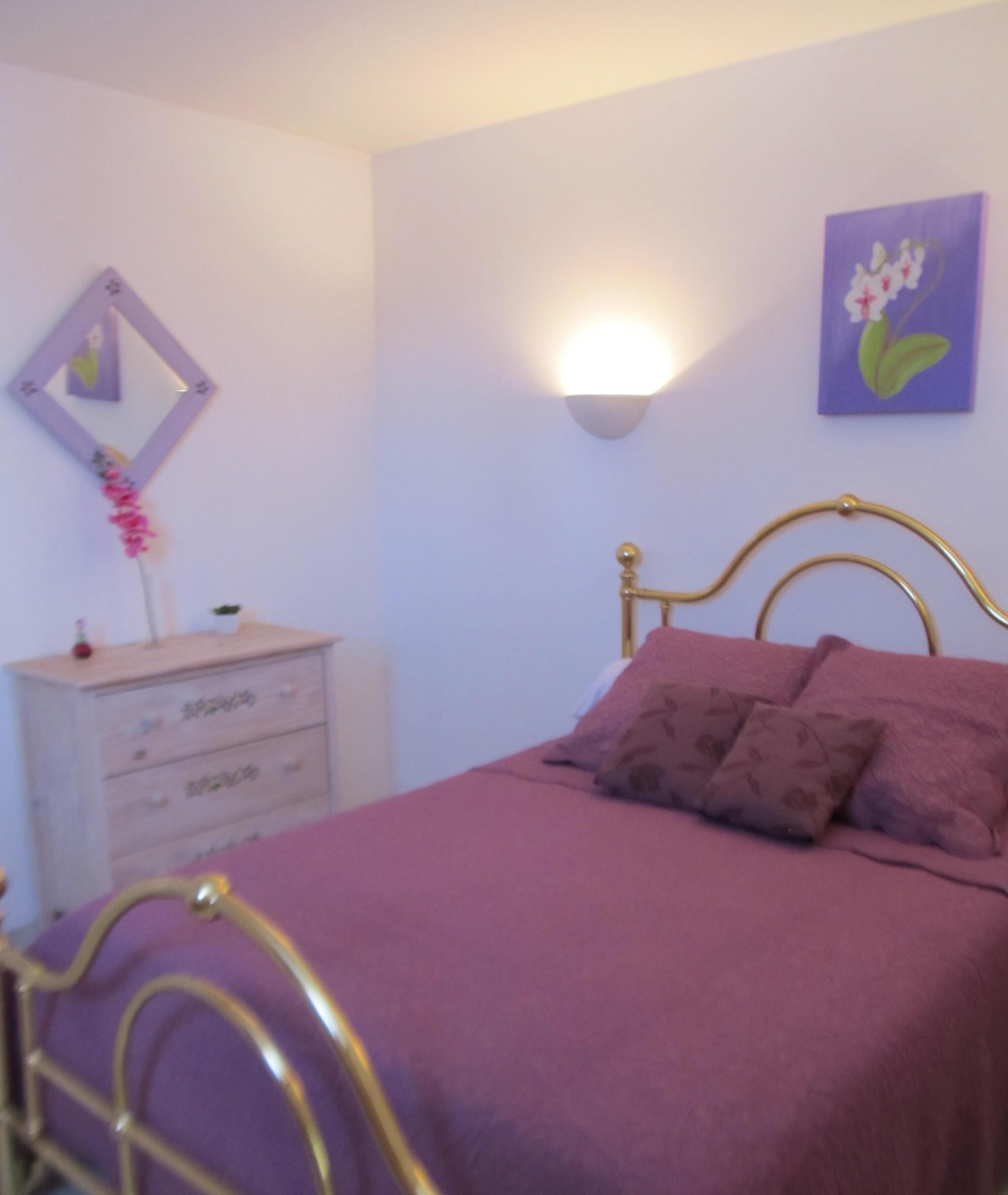 Une chambre à coucher comprenant un lit, une commode, une lampe fixée au mur et un tableau.