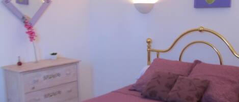 Une chambre à coucher comprenant un lit, une commode, une lampe fixée au mur et un tableau.
