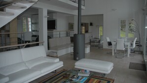 A spacious living area with a white sofa, a coffee table with books, a TV, and a staircase leading to an upper level.