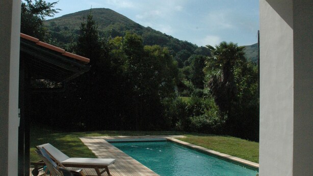 A pool area with two lounge chairs and a potted plant, surrounded by greenery and mountains.