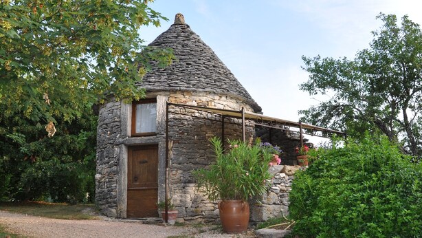 A stone cottage with a conical roof, a wooden door, and a small window.
