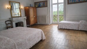 A room with two beds, a wooden cabinet, a fireplace, and a large window with a view. - L'intemporel, charming gîte in the Château de St Gervais, 4 to 5 people, 125m². (Saint-Gervais-La-Forêt)