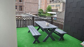 Eine Dachterrasse mit Holztisch und -bänken, umgeben von einem schwarzen Zaun und einem grünen Kunstrasen.
