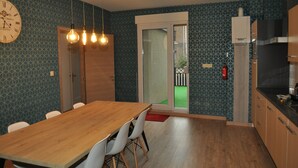 Eine moderne Küche mit einem Holztisch, weißen Stühlen, einer Uhr, Pendelleuchten und einer Glastür zum Balkon.