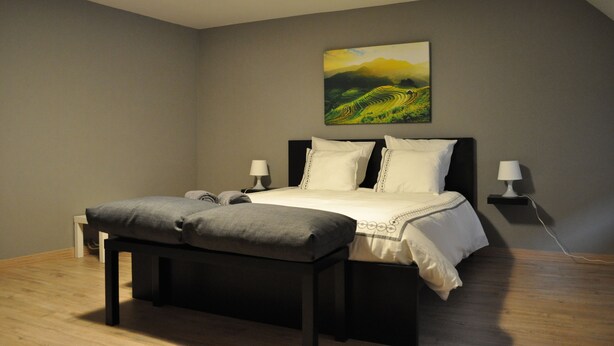 Ein Schlafzimmer mit Bett, Nachttischlampen, einer Bank und einem Bild an der Wand.