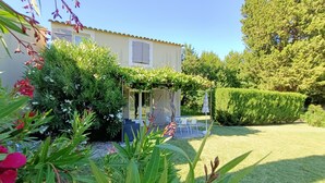 Ein Haus mit einer überdachten Terrasse, einem Rasen und unterschiedlichen Pflanzen.