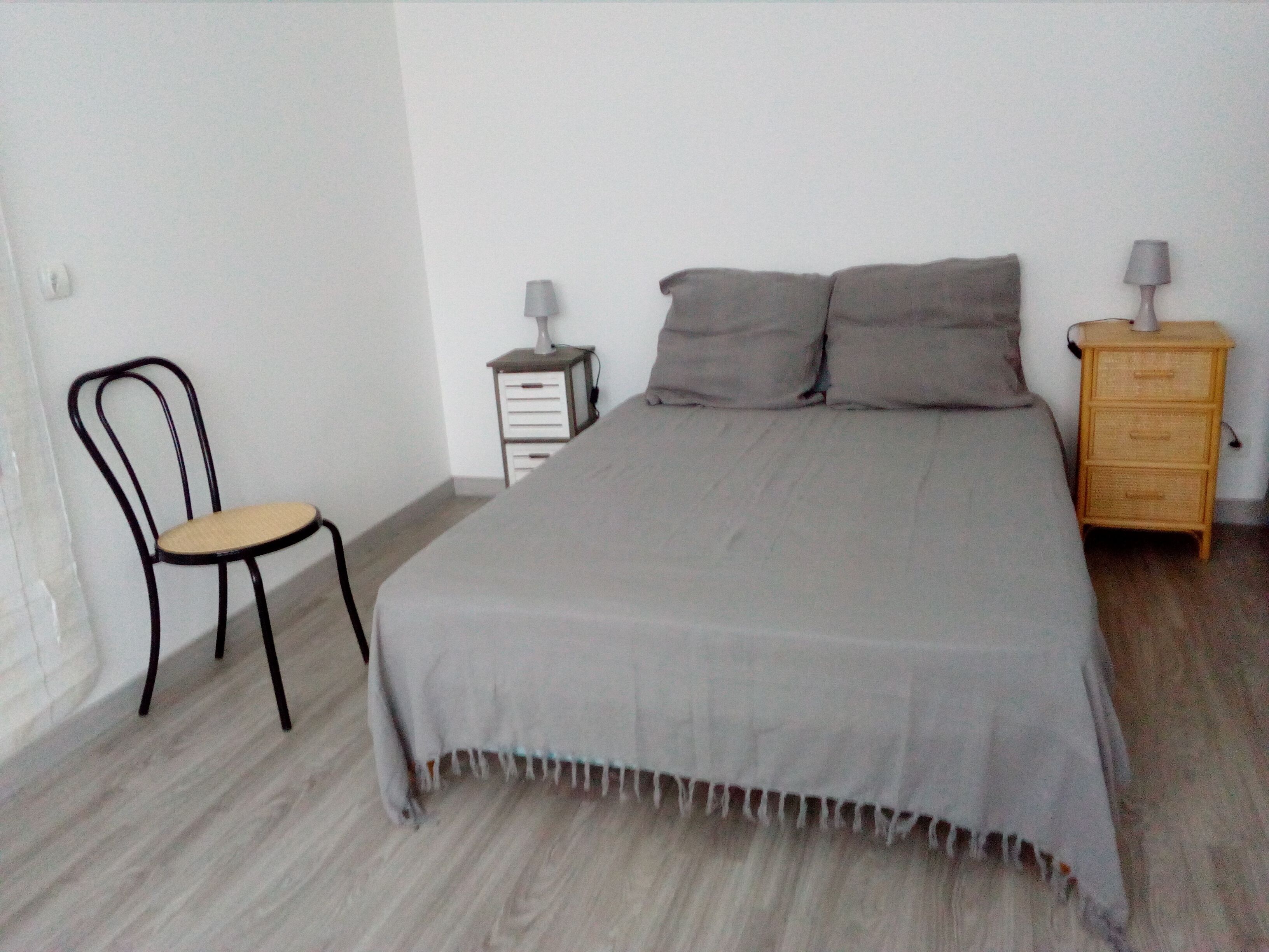 A bedroom with a bed, a chair, a nightstand, and a lamp.