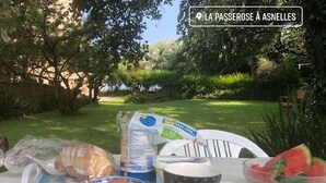 Une table avec des plats et une tasse, installée à l’extérieur, avec vue sur un jardin.