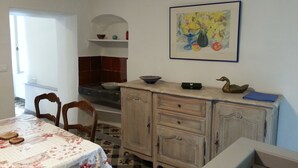 Un coin repas avec une table dressée pour deux personnes, une chaise en bois, un meuble avec des tiroirs et un tableau accroché au mur.