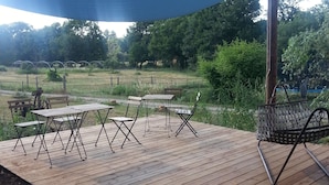 Une terrasse en bois avec des tables et des chaises en métal, un grand parasol bleu et une chaise en métal.