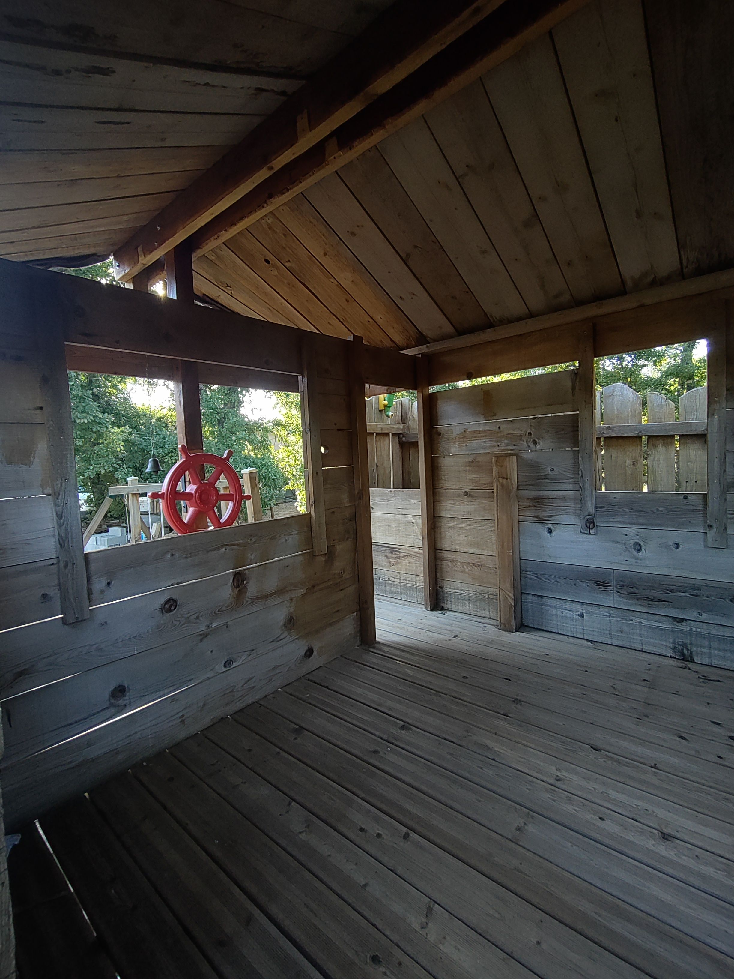 A wooden cabin with a sloped roof, a red steering wheel on the left, and a wooden deck.