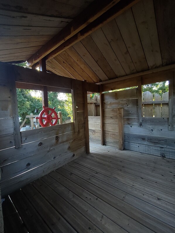 A wooden cabin with a sloped roof, a red steering wheel on the left, and a wooden deck.