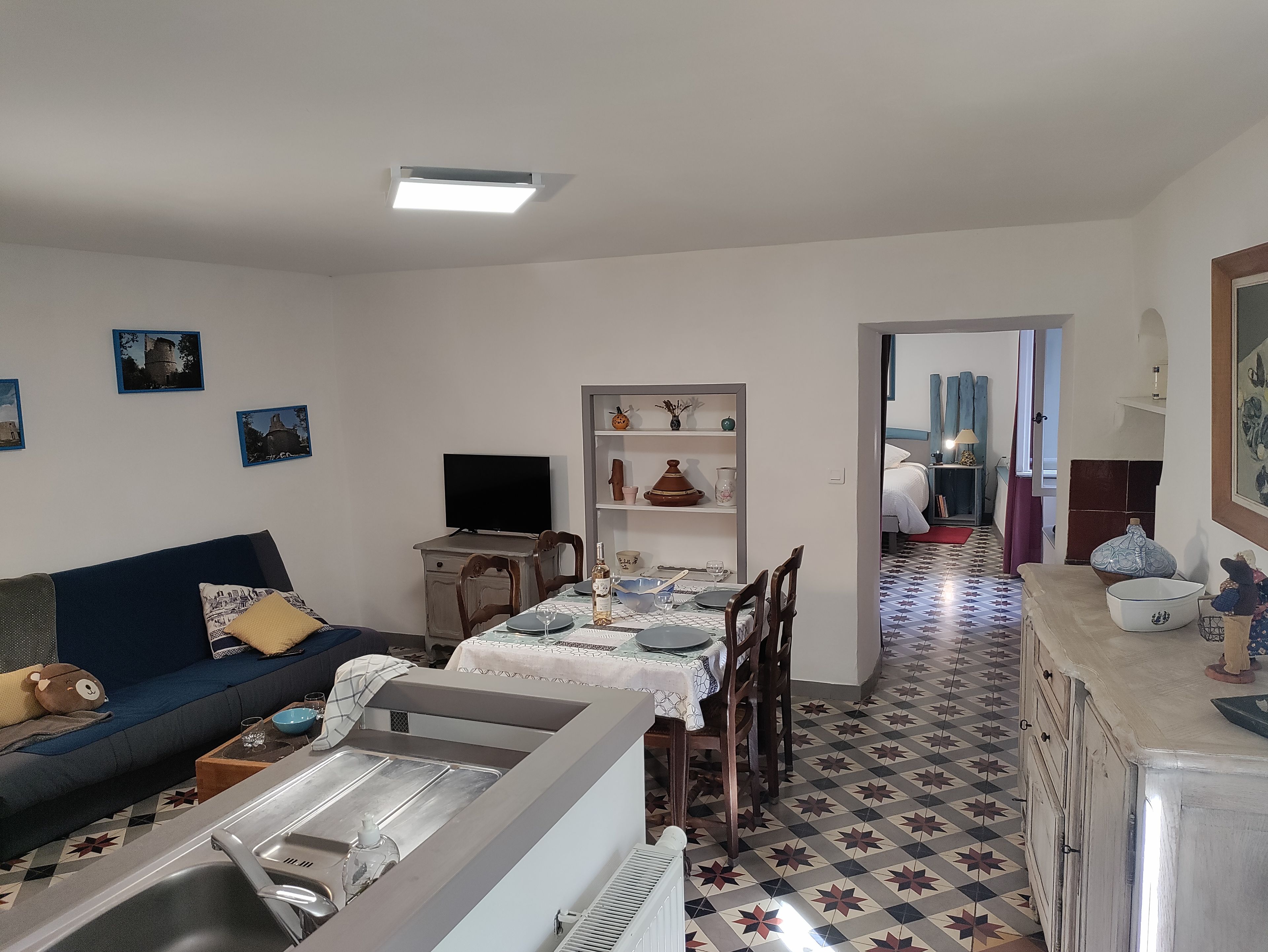 A living room with a sofa, a television, a dining table with chairs, and a kitchen area with a sink and cabinets.