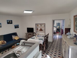 A living room with a sofa, a television, a dining table with chairs, and a kitchen area with a sink and cabinets.