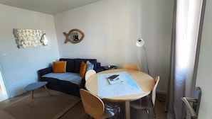 Una sala de estar moderna con una mesa redonda, un sofá y una mesa de centro. Hay un espejo decorativo en la pared y una lámpara de pie.