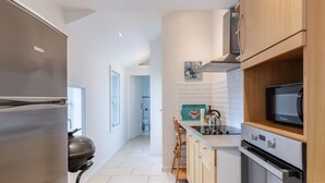 Una cocina moderna con un refrigerador de acero inoxidable, un microondas y un horno. Se aprecia un mueble de madera y una encimera con varios objetos.