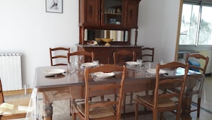 A dining area with a wooden table set for six, surrounded by wooden chairs. A wooden cabinet with glass doors is above the table, and there are framed pictures on the wall. - seasonal rental of a villa in the countryside (Meynes)