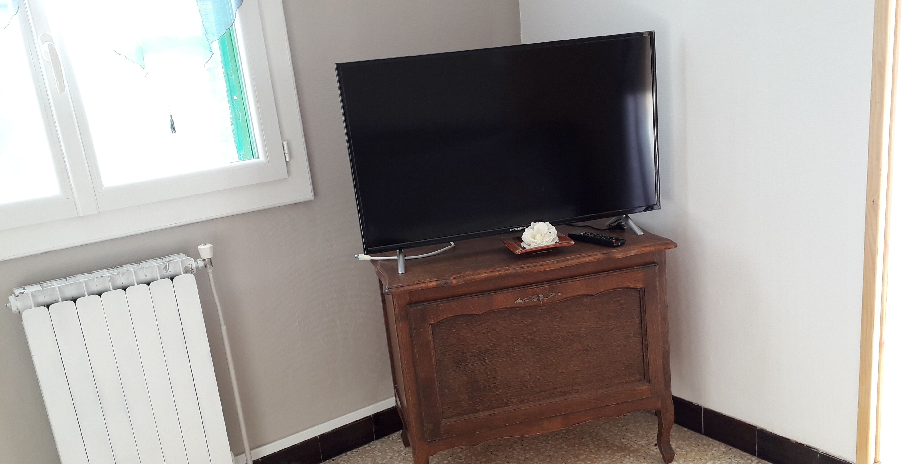 A television on a wooden stand in a room with a radiator and a window.