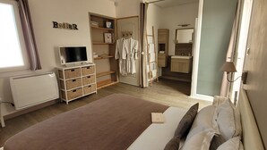 Een slaapkamer met een bed, een televisie, een kledingkast, een zichtbare badkamer door een open deur en een raam met gordijnen.