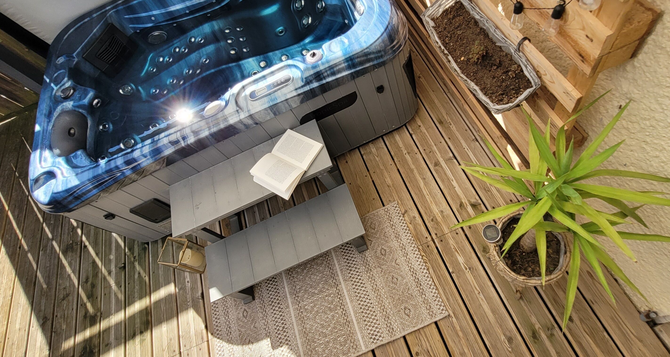 A hot tub, a book, a potted plant, and a wooden deck.