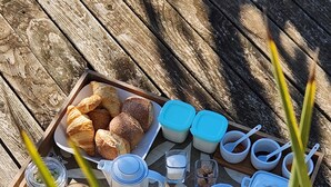Een houten dienblad met ontbijtartikelen, zoals croissants, een theepot, bekers en een glas sinaasappelsap.