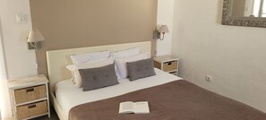 A neatly made bed with a brown blanket, two bedside tables with lamps, and a mirror on the wall.