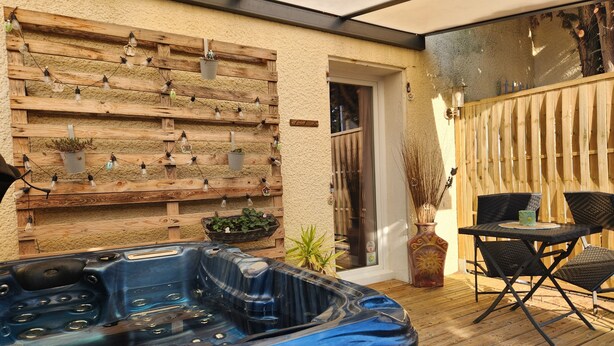Een hottub op een houten terras met een rustieke muur en tuinmeubilair.