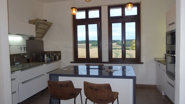 A modern kitchen with a central island, two bar stools, and a view of a field through large windows.