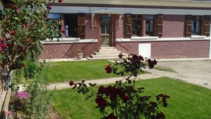 A brick building with a front entrance, a small garden with red roses, and a paved driveway.