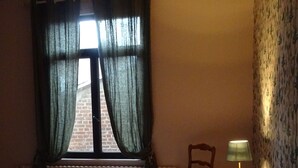 A bedroom with a bed, a chair, a window with curtains, a radiator, and a lamp on a side table.