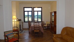 A dining area with a table set for four, flanked by wooden chairs. A brown leather sofa is positioned to the right.