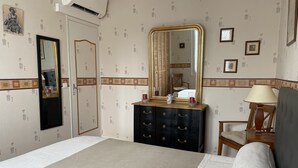 Ein Hotelzimmer mit Bett, Schminktisch, Sessel, Schreibtisch, Spiegel und Wand mit gemustertem Wandpapier.