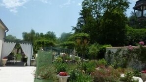 Ein Garten mit einer Patio, einem Pergola, Sitzgelegenheiten im Freien und verschiedenen Kübelpflanzen.