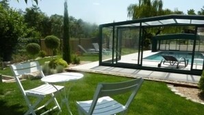 Eine verglaste Terrasse mit Pool, umgeben von einem gepflegten Rasen und einigen Stühlen.