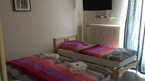 A bedroom with two single beds, a flat-screen TV mounted on the wall, and a window with curtains. - Gaststätte und Pension Frankenstube (Nidda)