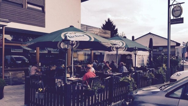 An outdoor seating area with tables and chairs, umbrellas, and a fence. - Gaststätte und Pension Frankenstube (Nidda)