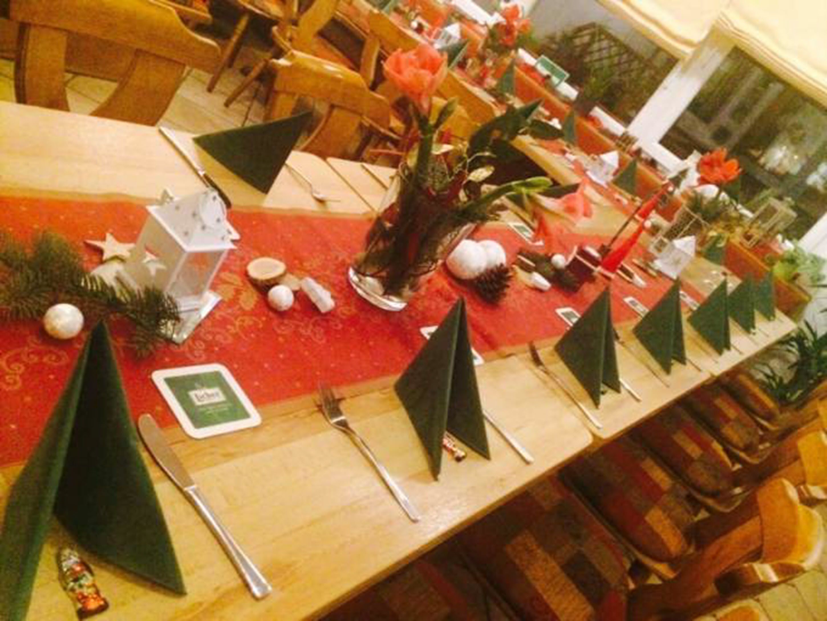 Una mesa de comedor con mantel rojo, decorada con adornos navideños, incluyendo una estrella, un pequeño árbol y un florero con flores.