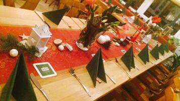 Una mesa de comedor con mantel rojo, decorada con adornos navideños, incluyendo una estrella, un pequeño árbol y un florero con flores.