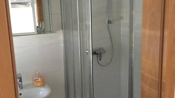 A bathroom with a glass shower enclosure, a sink, and a mirror.