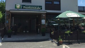 A building with a sign reading "SPEISEGASTSTATTE Frankenstube" and a green umbrella with the same logo. - Gaststätte und Pension Frankenstube (Nidda)