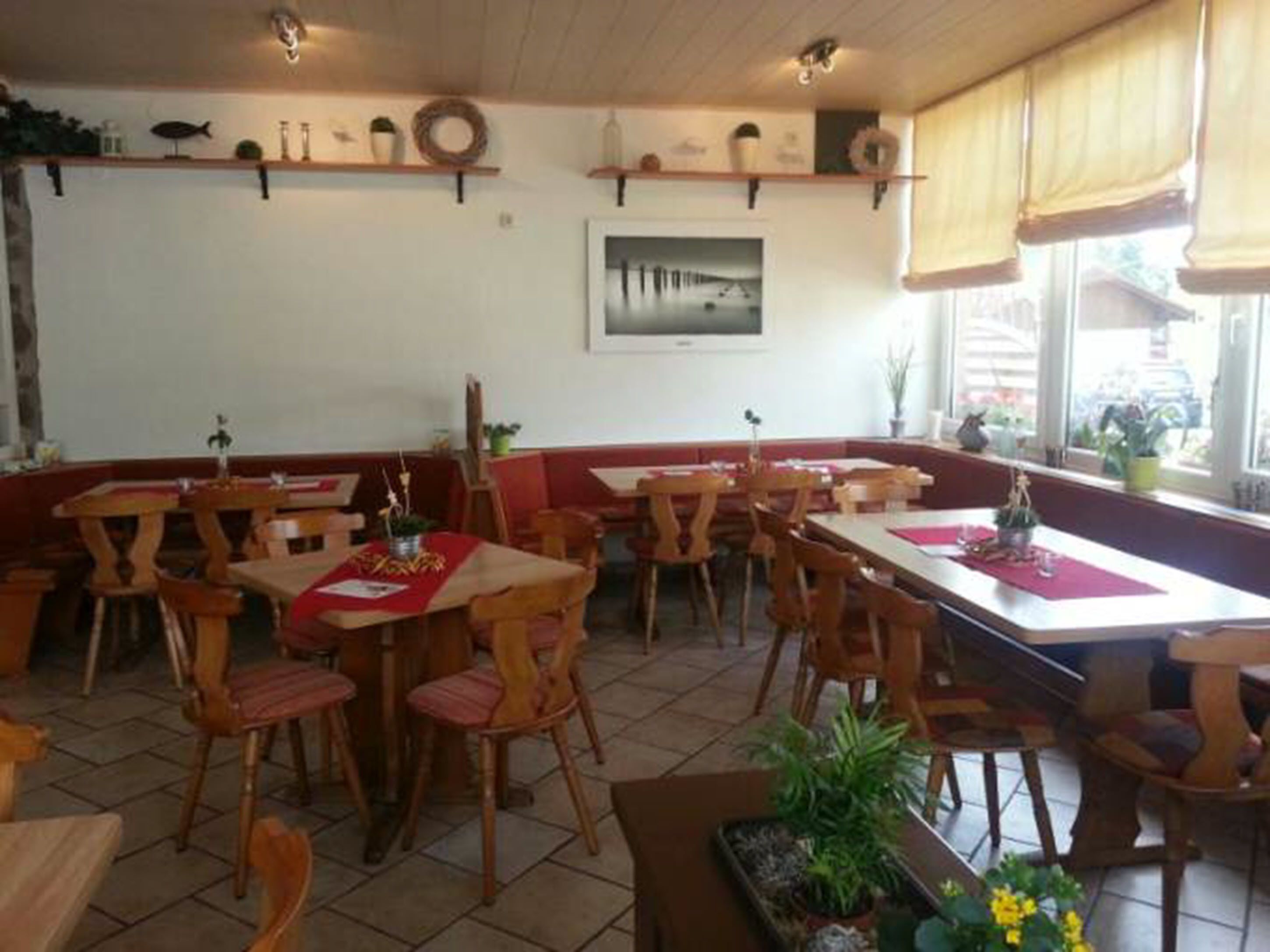 Ein Restaurant mit Holztischen und -stühlen, einem Fliesenboden und Blick auf die Außenwelt durch große Fenster.