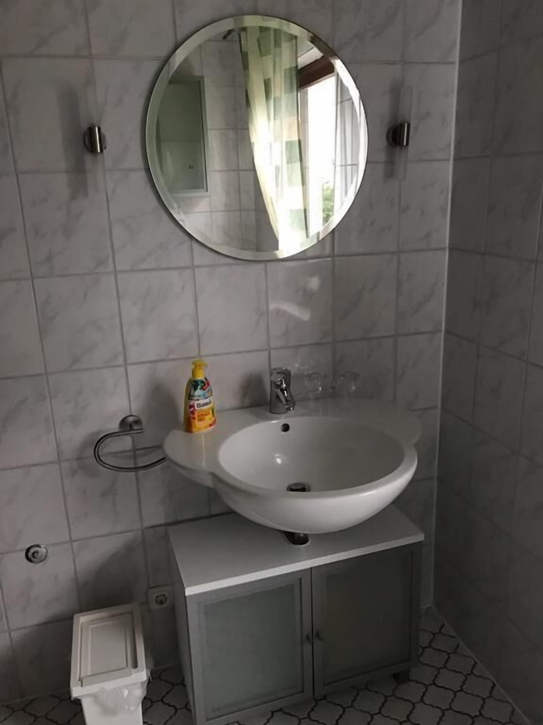 Un baño con un lavamanos blanco, un espejo redondo y un armario debajo.