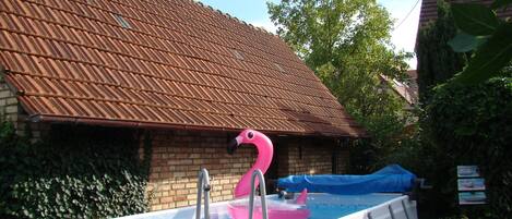A swimming pool with a pink flamingo float, surrounded by a brick building with a tiled roof.