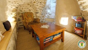 A cozy room with a stone wall, a wooden table with Scrabble games, a patterned armchair, and a bookshelf.