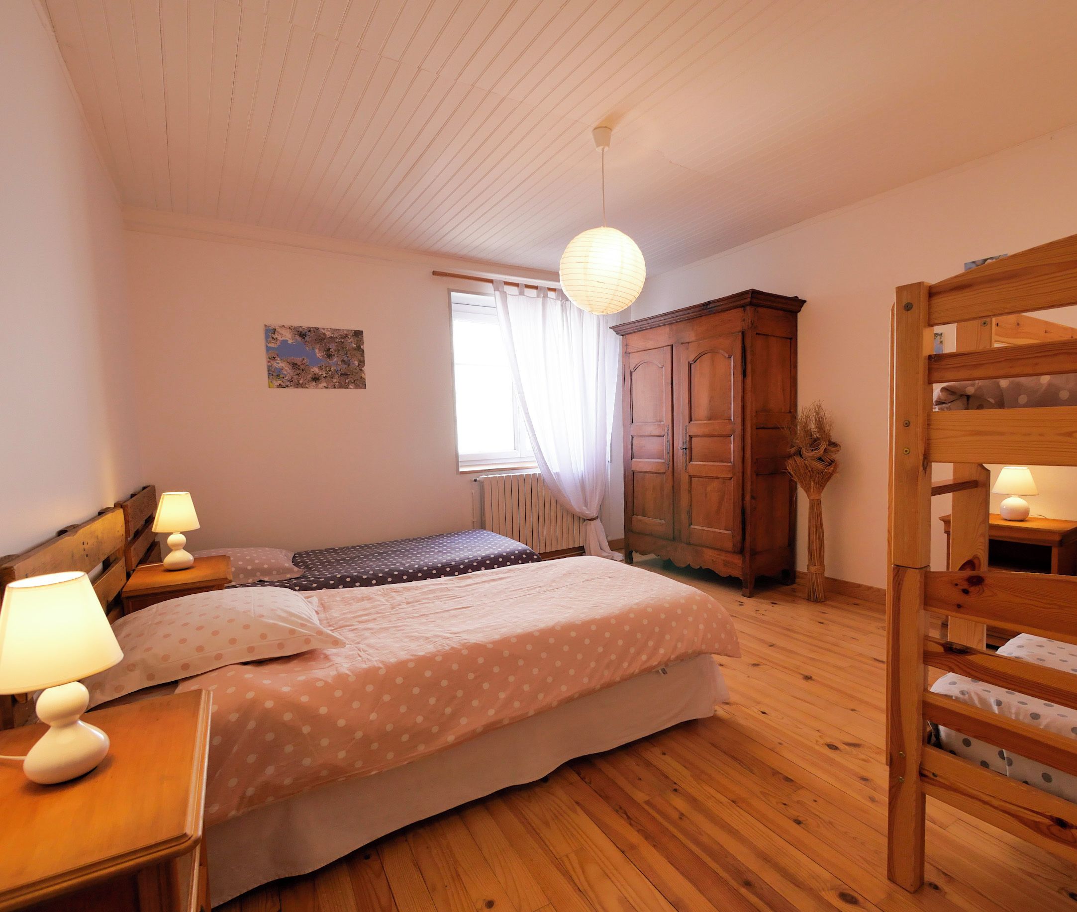 Ein Schlafzimmer mit einem Holzbett mit Etagen, einem Einzelbett, einem Holzschrank und einem Nachttisch mit Lampe.