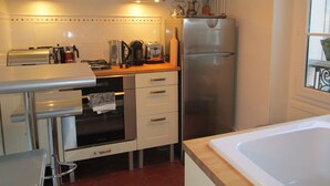A compact kitchen with a built-in oven, microwave, and a stainless steel refrigerator. There is a wooden countertop with various appliances and a window providing natural light. - Haven of peace in the center of Versailles (Versailles)
