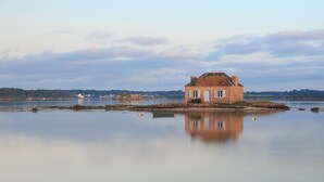 Uma casa pequena e isolada à beira de um lago calmo, com reflexo nítido.