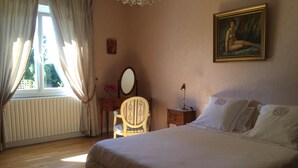 Quarto com uma cama grande, mesa de cabeceira de madeira com abajur, uma cadeira, cômoda e um quadro na parede.