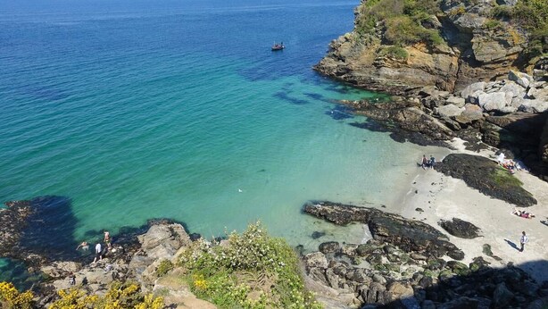 Paisagem costeira com águas turquesa cristalinas, falésias rochosas e uma praia arenosa.