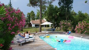 A pool area with lounge chairs, a wooden deck, and a house in the background. - Large villa with pool (Saint-Paul-En-Forêt)